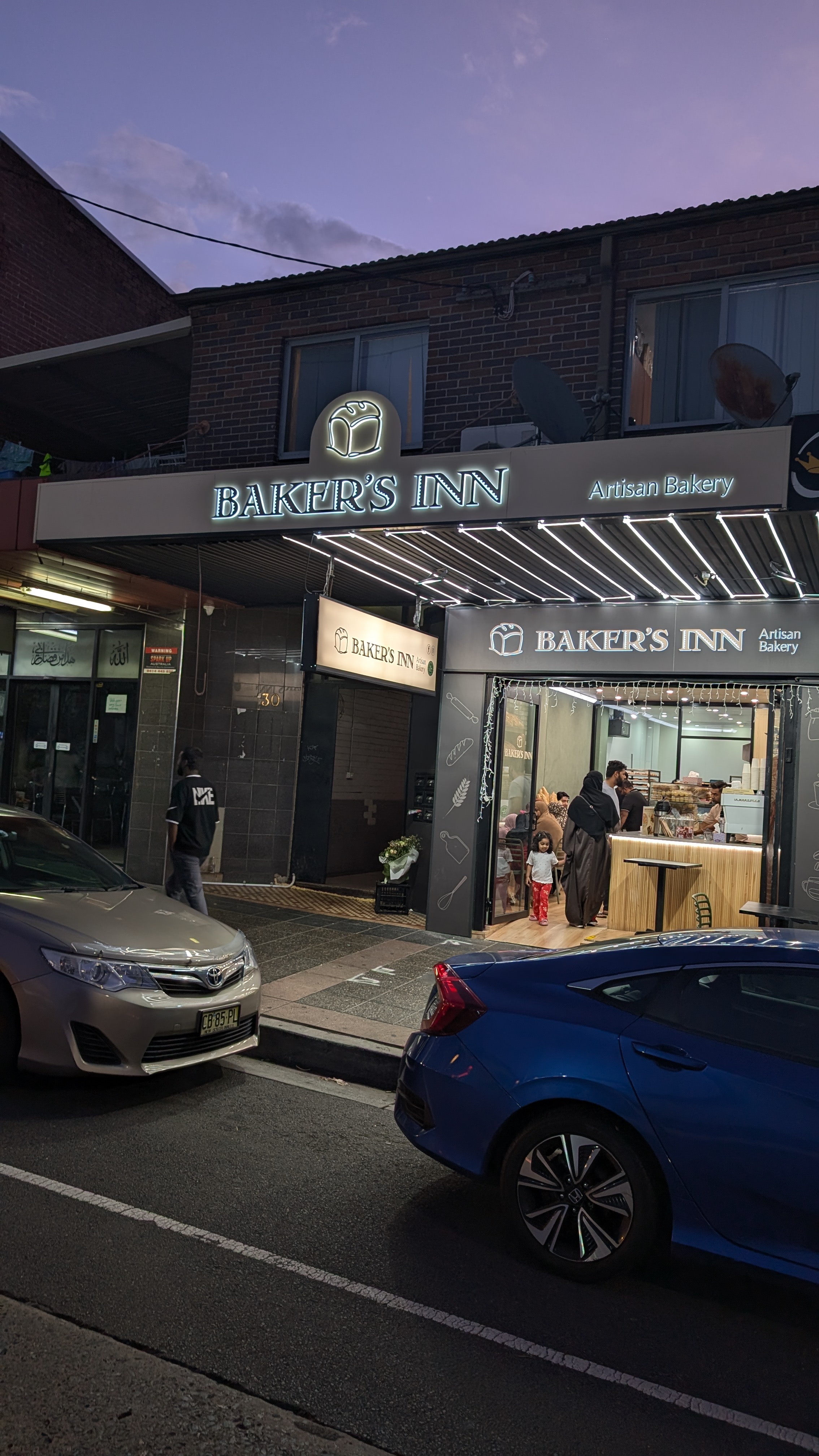 Baker’s Inn’s illuminated sign and welcoming entrance at dusk on Haldon Street, Lakemba